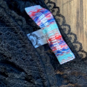 Peut inclure: Tissu en dentelle noire avec une &eacute;tiquette color&eacute;e qui indique "Free People" en blanc et bleu.