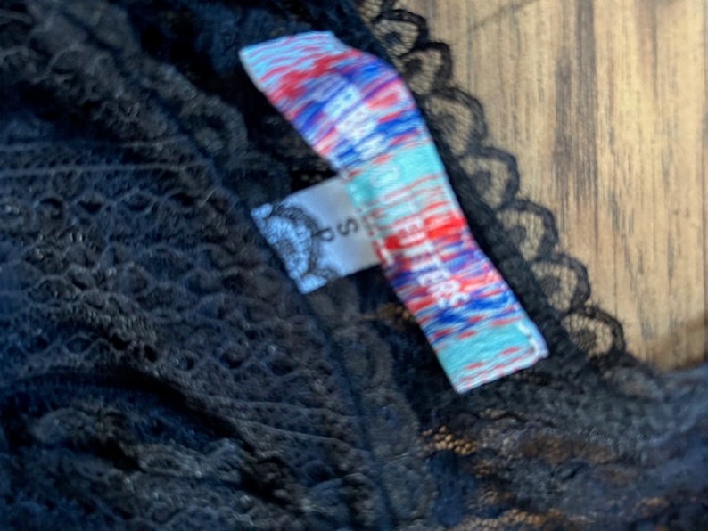 Peut inclure: Tissu en dentelle noire avec une &eacute;tiquette color&eacute;e qui indique "Free People" en blanc et bleu.
