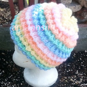 May include: A crocheted hat with a rainbow pattern in shades of pink, blue, and yellow. The hat is made with a textured, ruffled stitch.