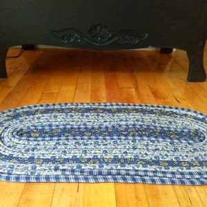 May include: A blue and white oval braided rug with a floral pattern. The rug is made of fabric scraps and is perfect for adding a touch of farmhouse charm to any room.