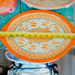 May include: An oval serving platter with an orange border and a floral design. The platter measures approximately 12 inches in length. The interior of the platter is white with orange and teal floral patterns.