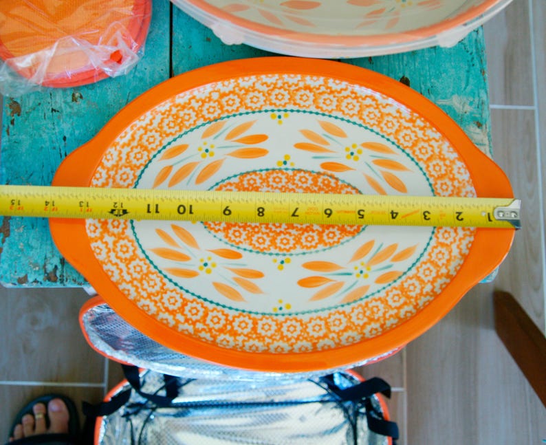May include: An oval serving platter with an orange border and a floral design. The platter measures approximately 12 inches in length. The interior of the platter is white with orange and teal floral patterns.
