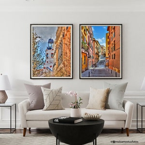 May include: A living room interior with a white sofa, two black end tables with lamps, and two framed photographs of cityscapes. The room is decorated with throw pillows, a potted plant, and a coffee table with a book on top.