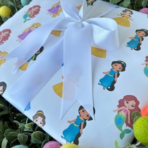 Pu&ograve; includere: Carta da regalo bianca con un fiocco di raso bianco. La carta presenta un motivo ripetuto di principesse Disney, tra cui Ariel, Belle, Jasmine e Rapunzel.