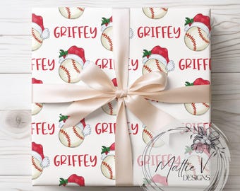 May include: White wrapping paper with a repeating pattern of baseballs wearing Santa hats and the name "GRIFFEY" printed in red. The paper is tied with a cream-colored ribbon.
