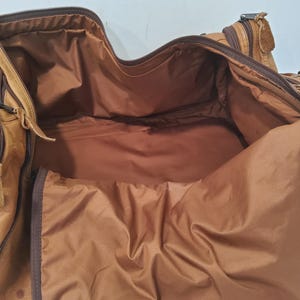 May include: Open view of a brown leather duffel bag. The bag has multiple zippered compartments and a spacious interior. The interior lining is a lighter shade of brown. The bag appears to be well-worn, with visible signs of use.