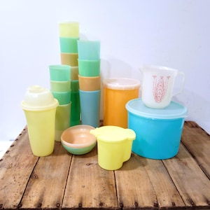 May include: A collection of vintage plastic kitchenware in various colors, including yellow, green, orange, and blue. The assortment features cups, bowls, a pitcher, and containers with lids, arranged on a wooden surface.