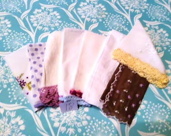 May include: A collection of vintage handkerchiefs in various colors and patterns. The handkerchiefs include white, purple polka dot, and brown with floral embroidery. Some have lace or crochet trim. The background is a blue and white floral pattern.