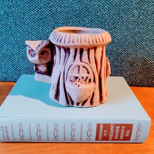 May include: A ceramic owl planter shaped like a tree stump with a small birdhouse opening and a bird inside. The planter is painted in shades of brown and beige.