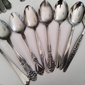 May include: A set of eight silver spoons with ornate handles. The spoons have a polished finish and are arranged in a fan shape.