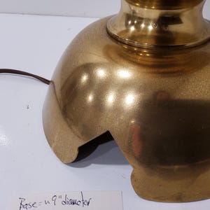 May include: A gold-colored lamp base with a rounded, textured design. The base has a 9-inch diameter and a cut-out section. A brown electrical cord extends from the base.