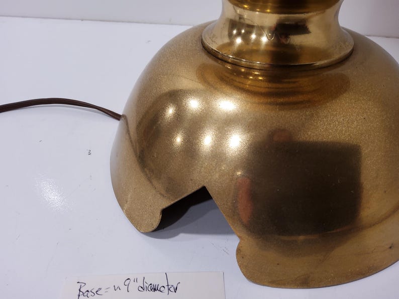 May include: A gold-colored lamp base with a rounded, textured design. The base has a 9-inch diameter and a cut-out section. A brown electrical cord extends from the base.
