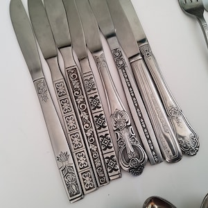 May include: A set of silver knives with intricate floral and geometric designs etched into the handles.