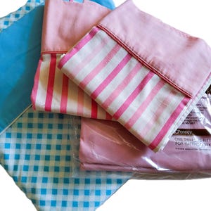 May include: Assortment of bed sheets in various patterns and colors. Includes a blue gingham sheet, a pink sheet, and a pink and white striped pillowcase. One sheet set is in a plastic package. The package text reads "ONE TWIN FITTED SET FOR MATTRESS 39x75 IN (99x190 CM)".