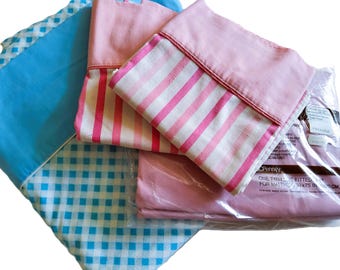 May include: Assortment of bed sheets in various patterns and colors. Includes a blue gingham sheet, a pink sheet, and a pink and white striped pillowcase. One sheet set is in a plastic package. The package text reads "ONE TWIN FITTED SET FOR MATTRESS 39x75 IN (99x190 CM)".