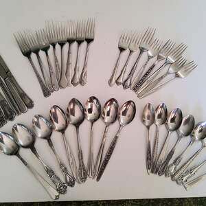 May include: A set of silverware with ornate handles, including forks, spoons, and knives. The silverware is made of stainless steel and has a polished finish.