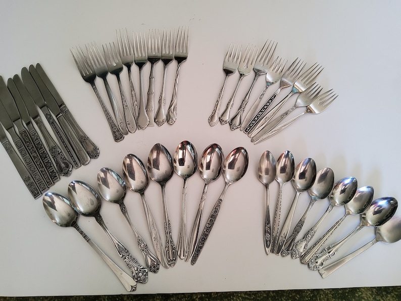 May include: A set of silverware with ornate handles, including forks, spoons, and knives. The silverware is made of stainless steel and has a polished finish.
