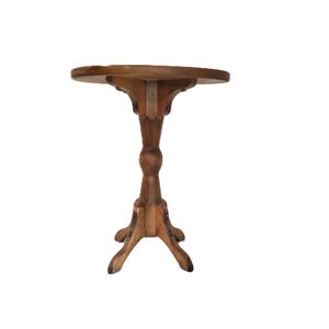 May include: A small, round, wooden side table with a pedestal base. The table has a dark brown finish and ornate carvings on the legs and the underside of the tabletop. The table stands approximately 28 inches tall.