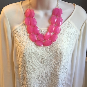 May include: A pink statement necklace with large, faceted beads. The necklace is made of multiple strands of beads and has a gold chain.