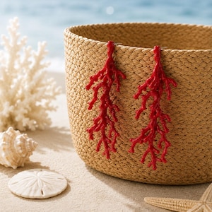 Puede incluir: Un par de pendientes de color rojo brillante con forma de estructuras de coral ramificadas. Los pendientes presentan un diseño orgánico y texturizado que imita la apariencia del coral natural, con múltiples protuberancias delicadas.