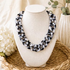 May include: A chunky chain link necklace featuring a marbled pattern of black and white acrylic links. The necklace consists of large, interlocking oval-shaped components that create a bold, continuous loop design around the neck display form.