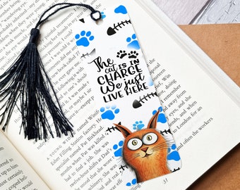 May include: A blue and white bookmark with a cartoon cat and the text "The cat is in charge we just live here". The bookmark has a black tassel.
