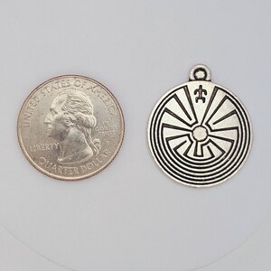 May include: Silver charm pendant featuring a Native American design with a spiral pattern and a symbol in the center. The charm is about the size of a US quarter.