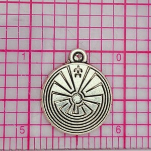 May include: Silver charm with a circular design featuring a labyrinth pattern and a turtle symbol in the center. The charm has a loop at the top for attaching to a necklace or bracelet.