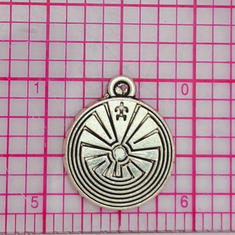 May include: Silver charm with a circular design featuring a labyrinth pattern and a turtle symbol in the center. The charm has a loop at the top for attaching to a necklace or bracelet.