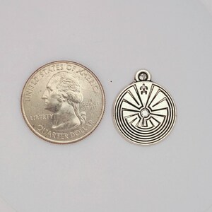 May include: Silver charm with a circular design featuring a sunburst pattern and a crystal in the center. The charm is about the size of a US quarter.
