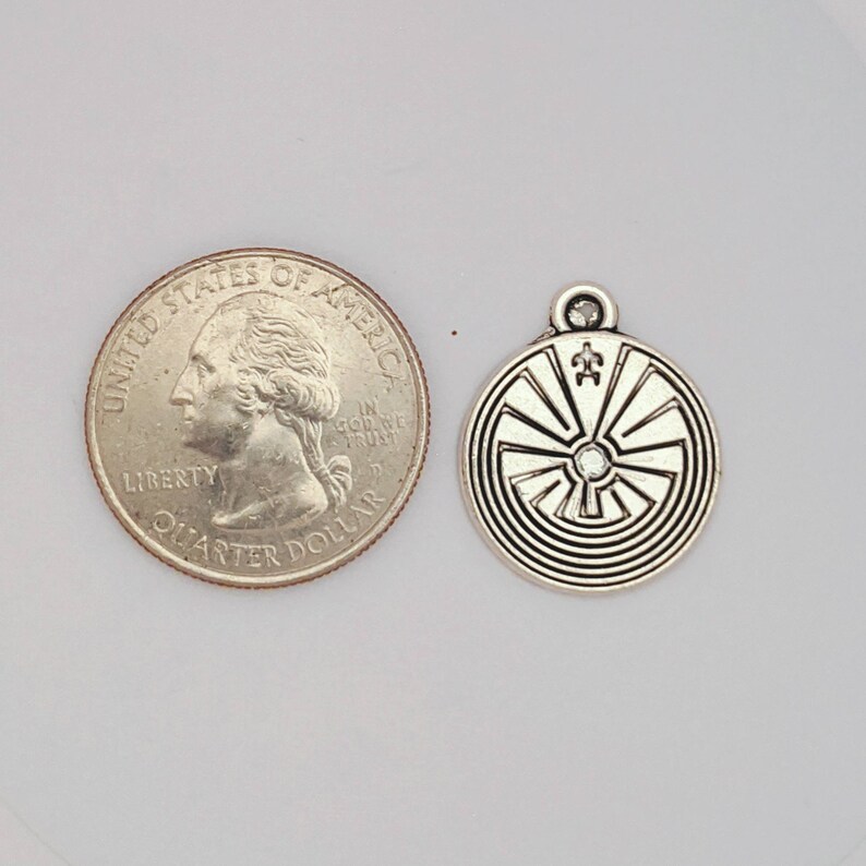 May include: Silver charm with a circular design featuring a sunburst pattern and a crystal in the center. The charm is about the size of a US quarter.
