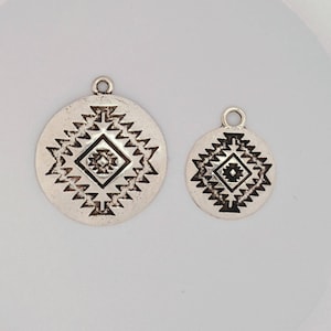 May include: Two silver charms with a geometric design. The larger charm is about 1 inch in diameter and the smaller charm is about 3/4 inch in diameter.