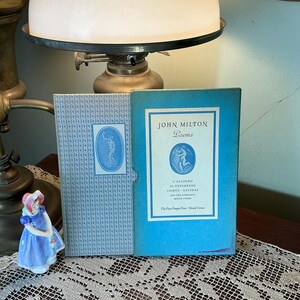 May include: Two vintage books, one light blue and one patterned, are displayed. The light blue book has the title "John Milton Poems" and a graphic. A small porcelain figurine of a woman in a blue dress is in the foreground.