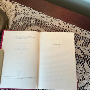 Puede incluir: Un libro abierto con una cubierta roja y p&aacute;ginas blancas. El texto de la p&aacute;gina izquierda dice "GORE VIDAL" y la p&aacute;gina derecha dice "For Lucien Price". El libro est&aacute; sobre una mesa con un camino de mesa de encaje.