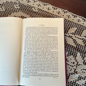 Puede incluir: Libro abierto con texto sobre una mesa con un mantel de encaje blanco. El texto incluye el t&iacute;tulo "A NOTE" y trata sobre la vida del emperador Juliano. Las p&aacute;ginas del libro son de color crema con texto negro.