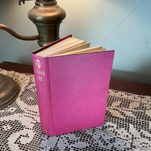 Puede incluir: Un libro de tapa dura rosa brillante, titulado "Julian Gore Vidal". El libro est&aacute; ligeramente abierto, revelando las p&aacute;ginas amarillentas. El libro est&aacute; sobre una mesa con un mantel de encaje, con una l&aacute;mpara de lat&oacute;n en el fondo.
