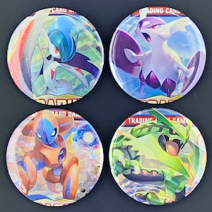 May include: Four round Pokemon Trading Card Game buttons. The buttons feature different Pokemon characters: Gardevoir, Sylveon, Metagross, and Sceptile. The buttons are white with a red border and the Pokemon Trading Card Game logo.