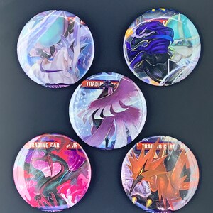 Könnte beinhalten: Fünf runde, bunte Knöpfe mit Pokémon-Charakteren. Die Knöpfe sind mit Bildern der Pokémon-Charaktere bedruckt, darunter ein lila und schwarzes Pokémon mit einer blauen Maske, ein weißes und blaues Pokémon mit einem blauen Horn, ein lila Pokémon mit einem weißen und rosa Schwanz, ein schwarzes und rotes Pokémon mit einem langen Hals und ein rotes und oranges Pokémon mit einem langen Schnabel.