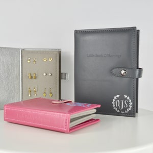 May include: Three earring storage boxes, one pink, one silver, and one gray. The gray box has the text "Little Book of Earrings" and the monogram "PJS" in a wreath.