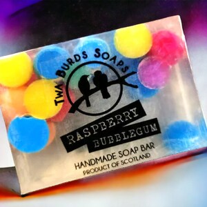 Peut inclure: Une barre de savon transparente avec un design color&eacute;. La barre de savon est d&eacute;cor&eacute;e de points ronds et color&eacute;s et porte le texte "Twa Birds Soaps", "Raspberry Bubblegum" et "Handmade Soap Bar Product of Scotland".