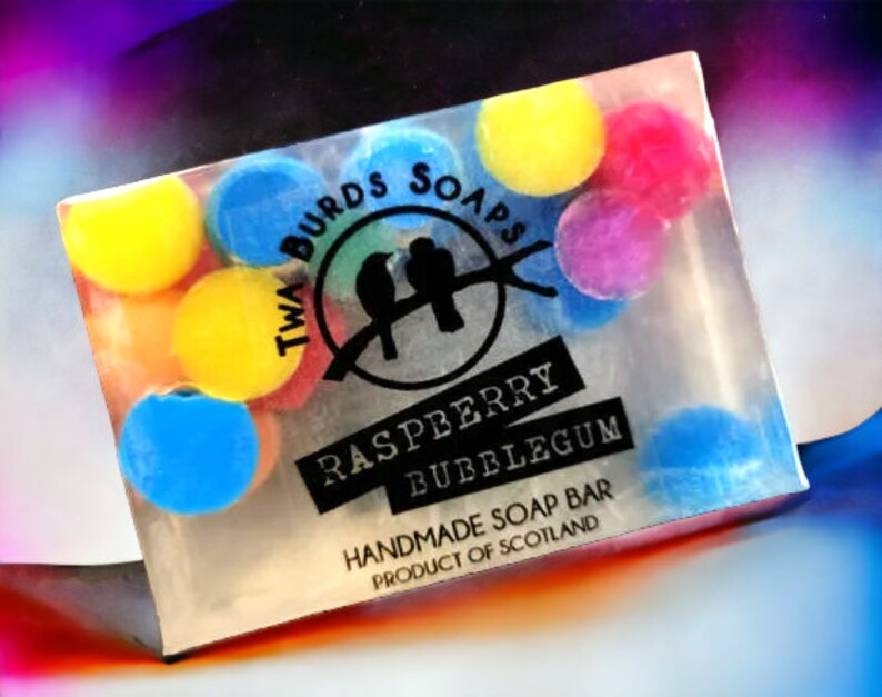 Peut inclure: Une barre de savon transparente avec un design color&eacute;. La barre de savon est d&eacute;cor&eacute;e de points ronds et color&eacute;s et porte le texte "Twa Birds Soaps", "Raspberry Bubblegum" et "Handmade Soap Bar Product of Scotland".