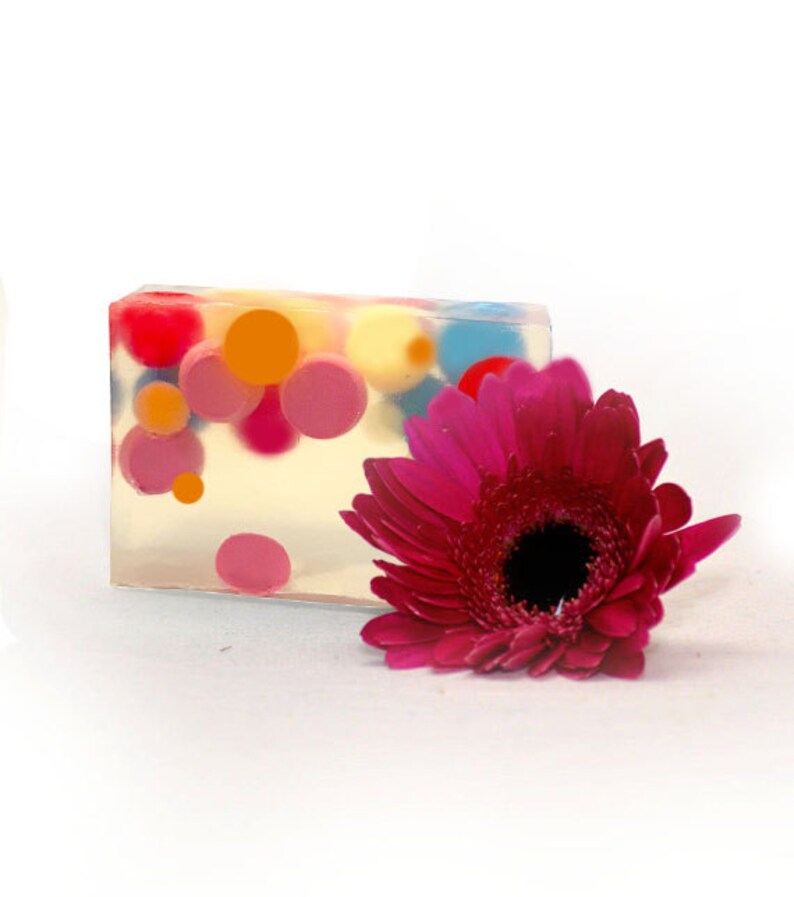 Peut inclure: Une barre de savon transparente avec des cercles color&eacute;s int&eacute;gr&eacute;s. Le savon est &agrave; c&ocirc;t&eacute; d'une gerbera rose.