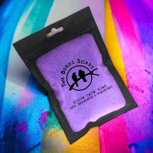 May include: A purple Epsom bath soak with a black resealable pouch. The pouch has a logo with two birds and the text "Twa Burds Soaps" and "Epsom Bath Soak No.32 Sandalwood & Frangipani".