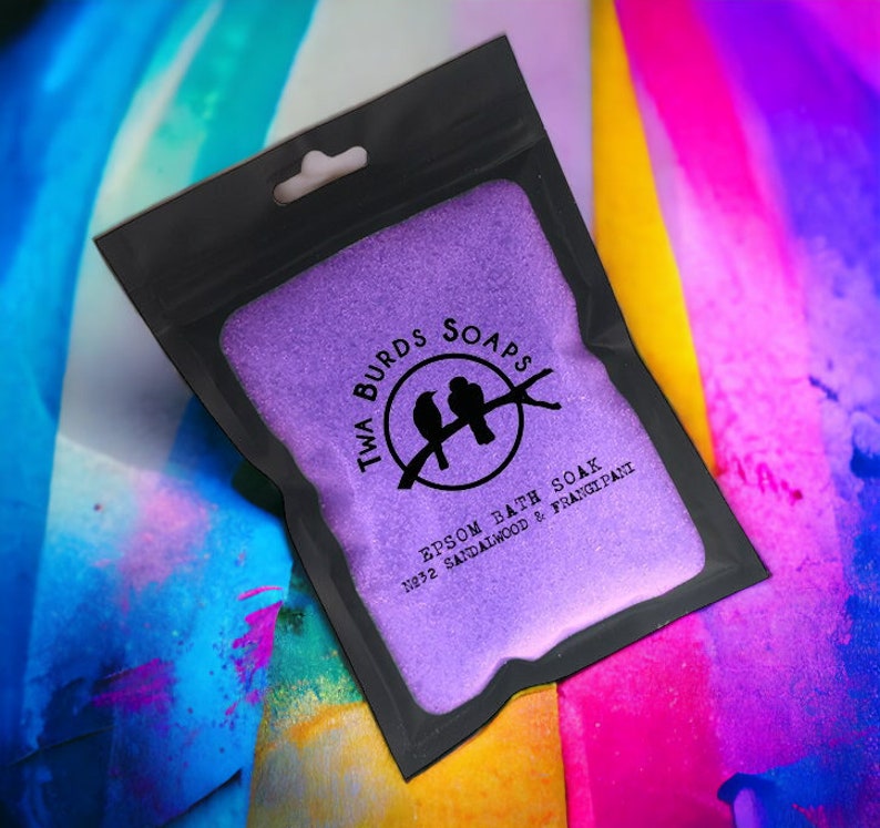 May include: A purple Epsom bath soak with a black resealable pouch. The pouch has a logo with two birds and the text "Twa Burds Soaps" and "Epsom Bath Soak No.32 Sandalwood & Frangipani".