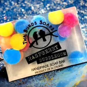 Peut inclure: Une barre de savon transparente avec un design color&eacute;. La barre de savon porte un logo qui dit "Twa Birds Soaps" et les mots "Raspberry Bubblegum" et "Handmade Soap Bar Product of Scotland".