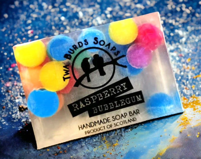 Peut inclure: Une barre de savon transparente avec un design color&eacute;. La barre de savon porte un logo qui dit "Twa Birds Soaps" et les mots "Raspberry Bubblegum" et "Handmade Soap Bar Product of Scotland".