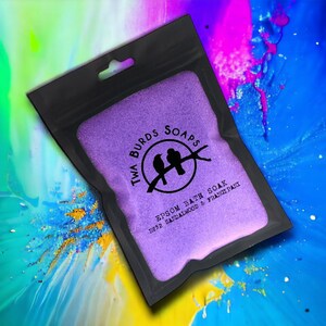 May include: A purple pouch with a black zipper and a white logo that says "Twa Burds Soaps" with two birds on a branch. The text below the logo says "Epsom Bath Soak No.32 Sandalwood & Frangipani".