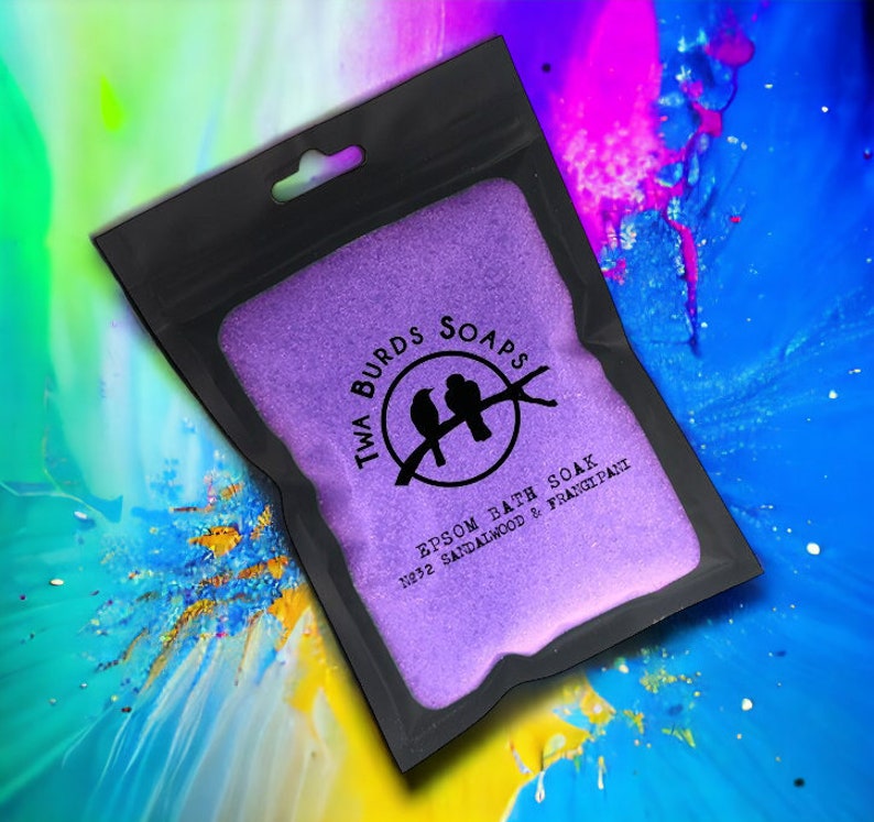 May include: A purple pouch with a black zipper and a white logo that says "Twa Burds Soaps" with two birds on a branch. The text below the logo says "Epsom Bath Soak No.32 Sandalwood & Frangipani".