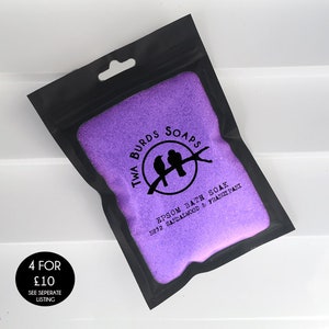 May include: A black resealable pouch filled with purple bath salts. The pouch has a white label with the text "Twa Burds Soaps" and a logo of two birds on a branch. The label also includes the text "Epsom Bath Soak 1932 Sandalwood & Frangipani".