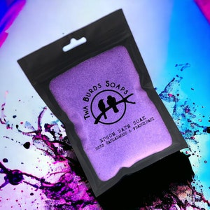 May include: A purple pouch with a black zipper and a white label that says "Twa Burds Soaps" with two birds on a branch and the text "Epsom Bath Soak No.32 Sandalwood & Frangipani".